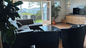 Una sala moderna con un sofá seccional, una mesa de centro y un televisor sobre un mueble de madera. Hay un ventanal con vistas al exterior.