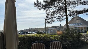 Un patio con dos sillas a rayas y una mesa, con vista a un estacionamiento y un edificio de techo inclinado.