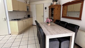 Een keuken met houten kastjes, een eettafel met zwarte stoelen en een bloevas.