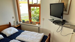 Een hotelkamer met twee bedden, een televisie op een standaard, een raam met uitzicht op groen en een kleine tafel met een lamp en decoratieve objecten.