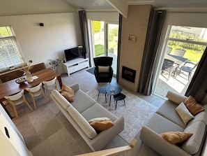 A modern living room with a sofa, a TV, a fireplace, and a dining area with a table and chairs.