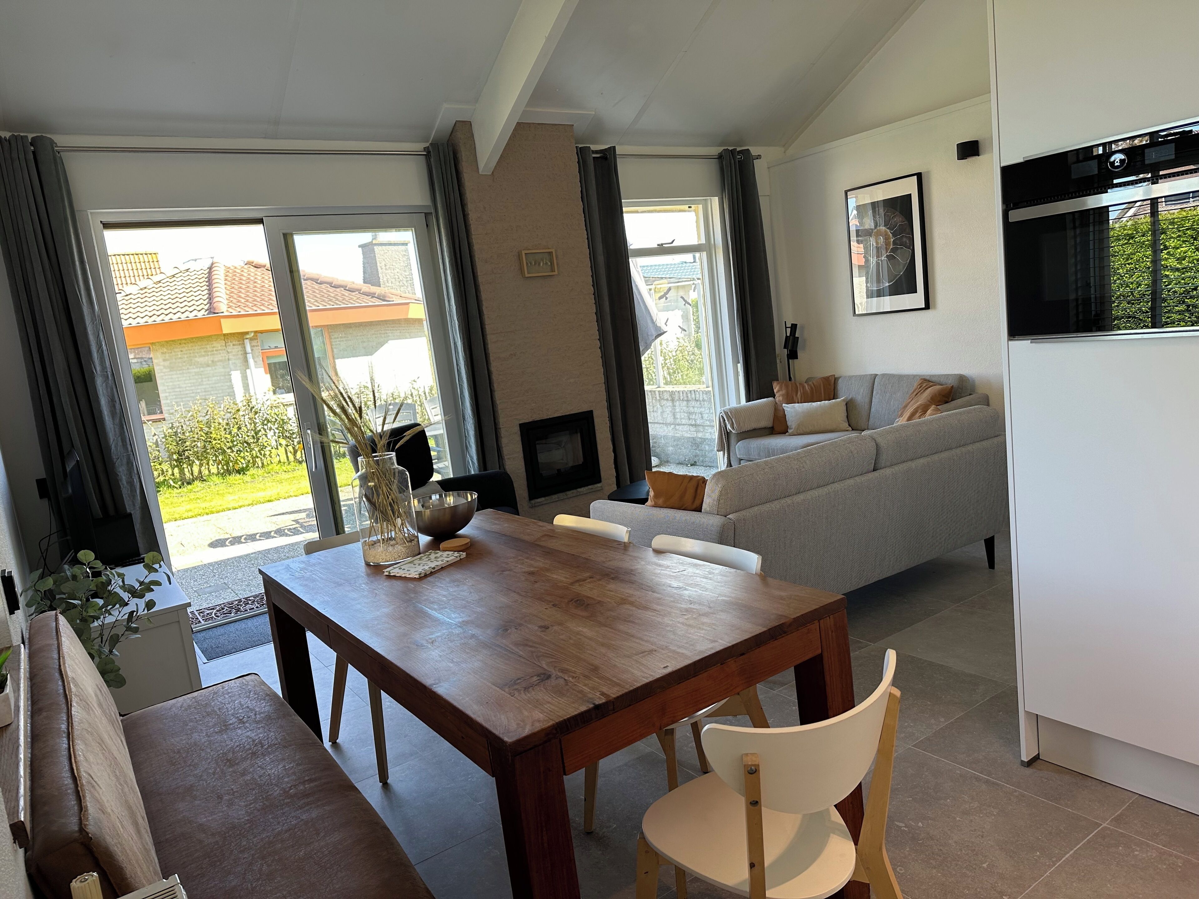 A modern living room with a sofa, a dining table with chairs, and a kitchen area with a refrigerator.