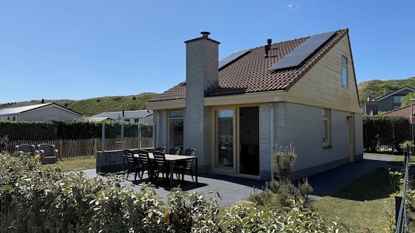 A two-story house with a tiled roof, a chimney, and a patio with a table and chairs.