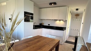 Een moderne keuken met witte kastjes, een houten eettafel en een vaas met gedroogde planten.