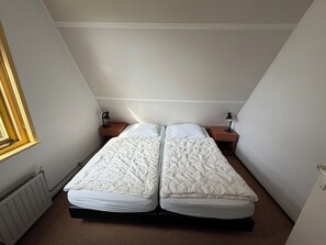 A small, single-room accommodation with two beds, a window, and a radiator.