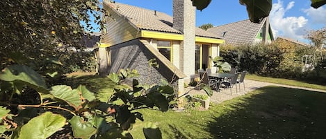 A house with a stone facade, a tiled roof, and a small patio with a table and chairs.