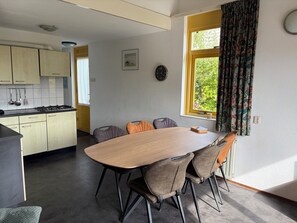 A dining area with a wooden table and four chairs, a kitchen with light-colored cabinets, and a window with curtains.