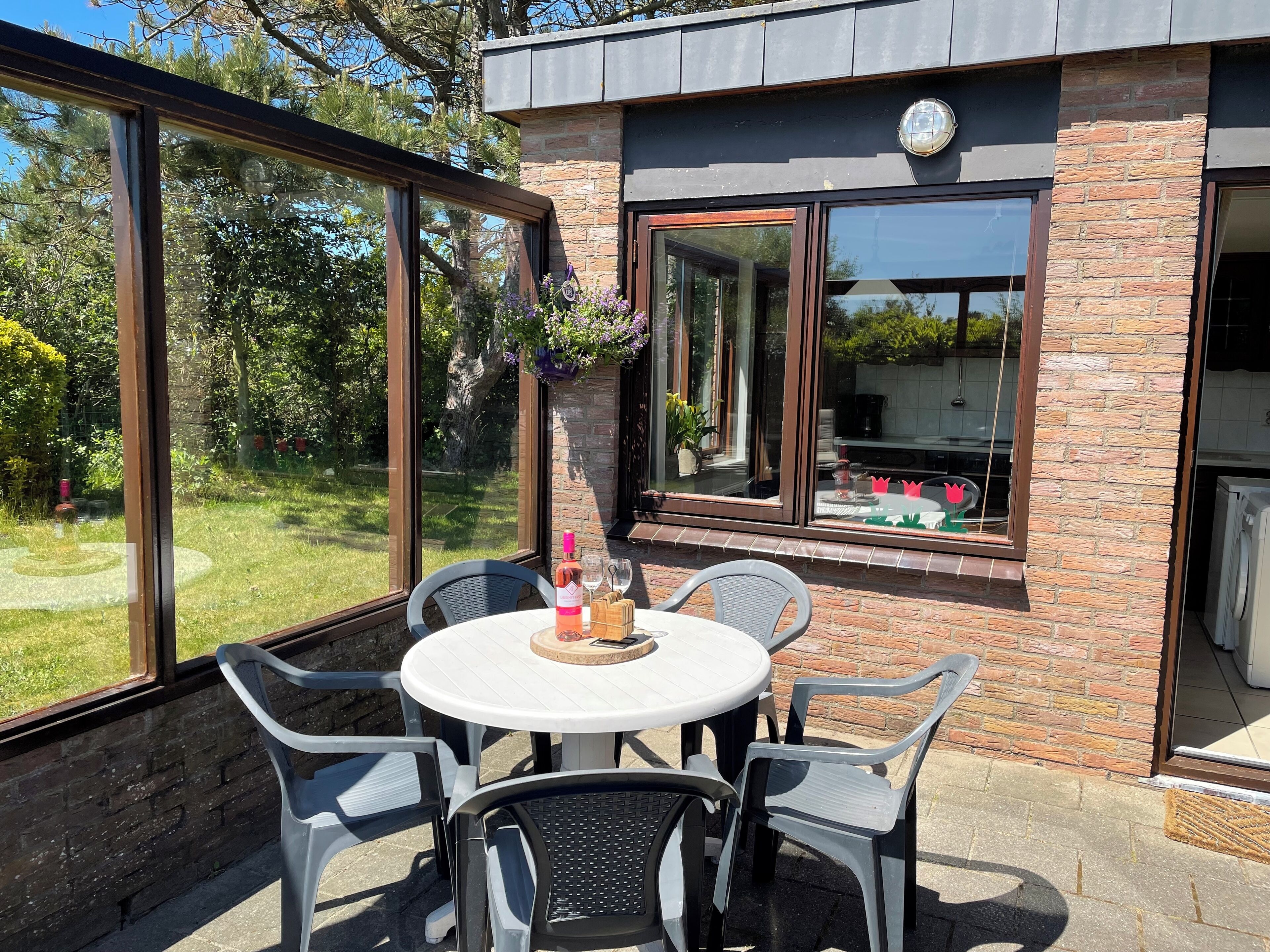 Een terras buiten met een ronde tafel en vier stoelen, een fles wijn en een glas op de tafel.