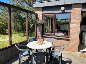 Een terras buiten met een ronde tafel en vier stoelen, een fles wijn en een glas op de tafel.