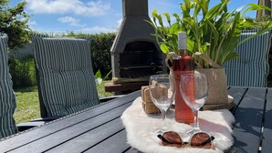 Une terrasse avec un four en pierre, une bouteille de vin, des verres et des chaises à rayures.
