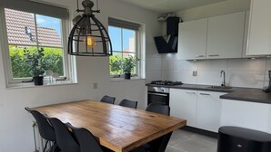 Une cuisine moderne avec des meubles blancs, une table à manger en bois, des chaises noires et une poubelle noire.