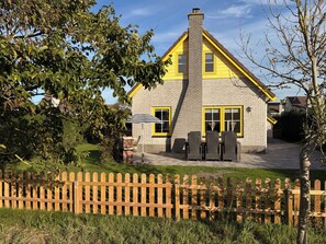 A two-story house with a brick exterior and yellow trim, a wooden fence in the foreground, and a clear sky. - 3 bedroom accommodation in Julianadorp aan Zee (Julianadorp aan Zee)