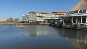 Een gebouw aan het water met een restaurantterras met uitzicht op een rustig wateroppervlak.