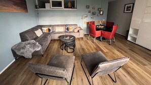 Een moderne woonkamer met een hoekbank, een ronde salontafel en een eethoek met rode stoelen.