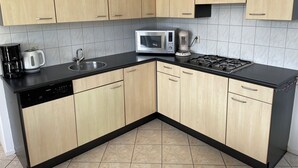 Een moderne keuken met lichte houten kastjes, een zwart aanrecht, een magnetron, een koffiezetapparaat en een vaatwasser.