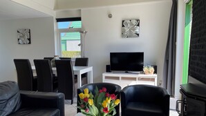Een moderne woonkamer met een bank, fauteuils, een salontafel met een bloevas, een televisie en een open haard.