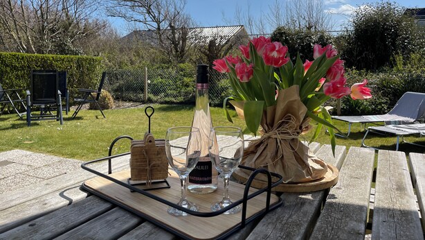 Een picknickopstelling met een houten tafel, een waterfles, een glas en een boeket roze tulpen.