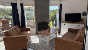 A living room with a fireplace, two sofas, a TV, and a dining table. - 3 bedroom accommodation in Julianadorp (Julianadorp)
