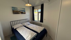 A small, clean room with a bed, a window with curtains, a painting on the wall, and a ceiling light. - 3 bedroom accommodation in Julianadorp (Julianadorp)