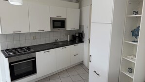 A modern kitchen with white cabinets, a black countertop, a built-in oven, a microwave, and a coffee maker. - 3 bedroom accommodation in Julianadorp (Julianadorp)
