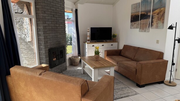 A living room with a brick fireplace, a sofa, a coffee table, and a TV on a cabinet. - 3 bedroom accommodation in Julianadorp (Julianadorp)