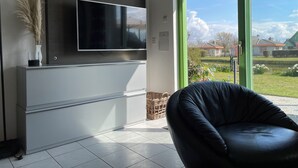 Una sala de estar moderna con un televisor de pantalla plana montado en la pared, un sillón de cuero negro y vista a un jardín por una ventana grande.