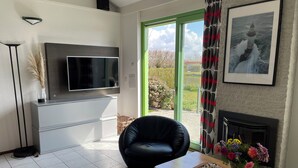 Una sala de estar con televisor, chimenea, un sillón cómodo y una mesa con flores.