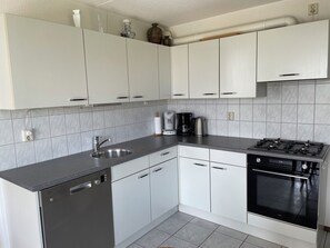 A modern kitchen with white cabinets, a stainless steel sink, a Bosch dishwasher, a coffee maker, and a black stove.