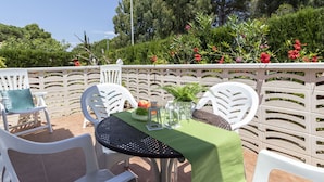 Eine Terrasse im Freien mit weißen Stühlen und einem Tisch, der mit einer grünen Tischdecke bedeckt ist, umgeben von einem weißen Zaun und üppigem Grün.