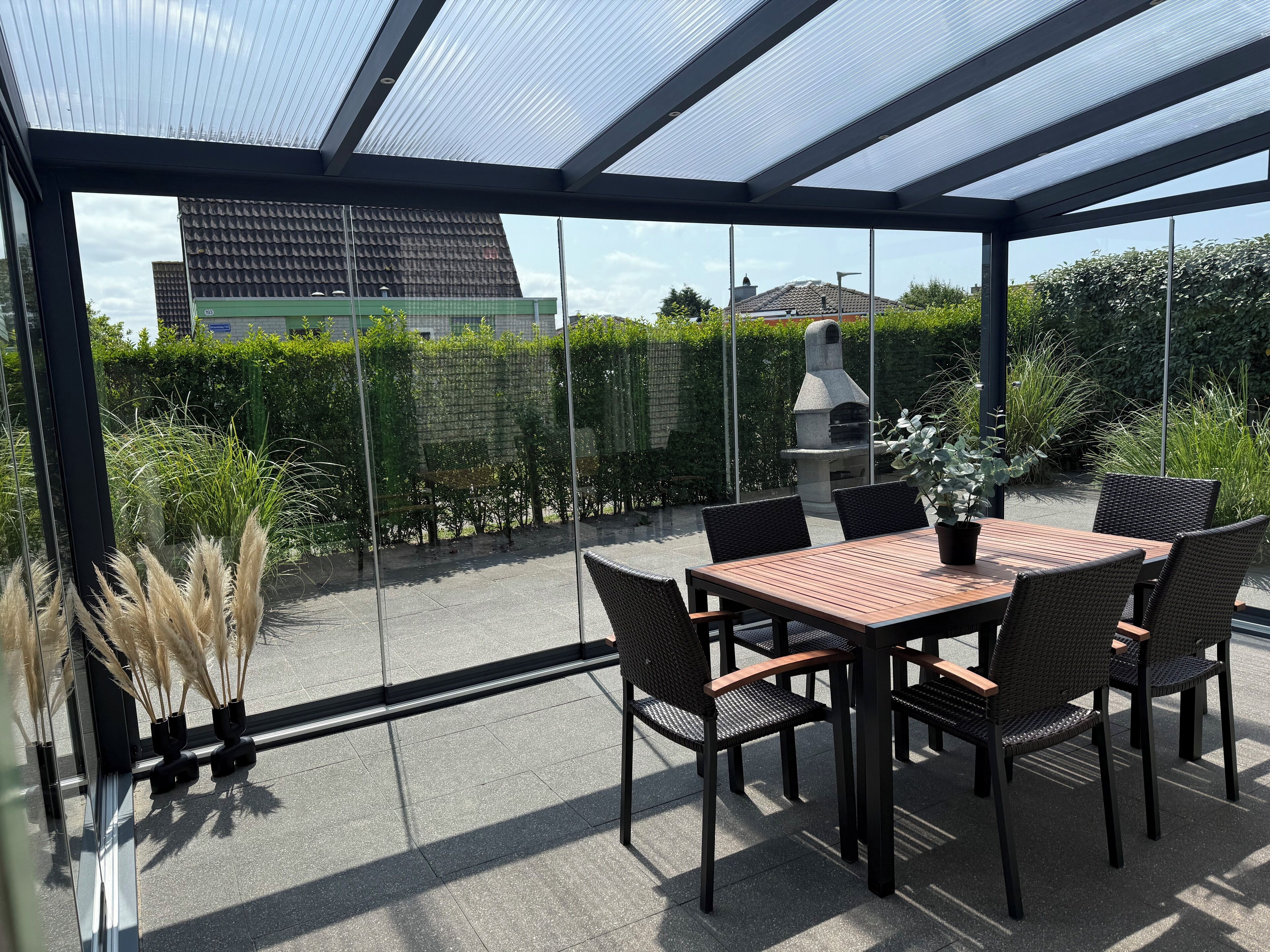 Eine überdachte Terrasse mit Tisch und Stühlen, einem Grill und Blick auf eine Stadtlandschaft.