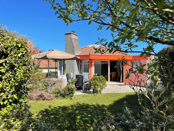 A house with a stone chimney, a covered patio, and a well-maintained garden.