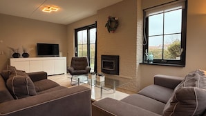 A living room with a sofa, armchair, TV, fireplace, and large windows. - 3 bedroom accommodation in Julianadorp aan Zee (Julianadorp aan Zee)