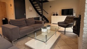 A modern living room with a sofa, a glass coffee table, a TV, and a fireplace. - 3 bedroom accommodation in Julianadorp aan Zee (Julianadorp aan Zee)
