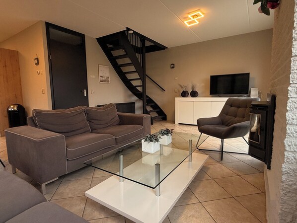 A modern living room with a sofa, a glass coffee table, a TV, and a fireplace.