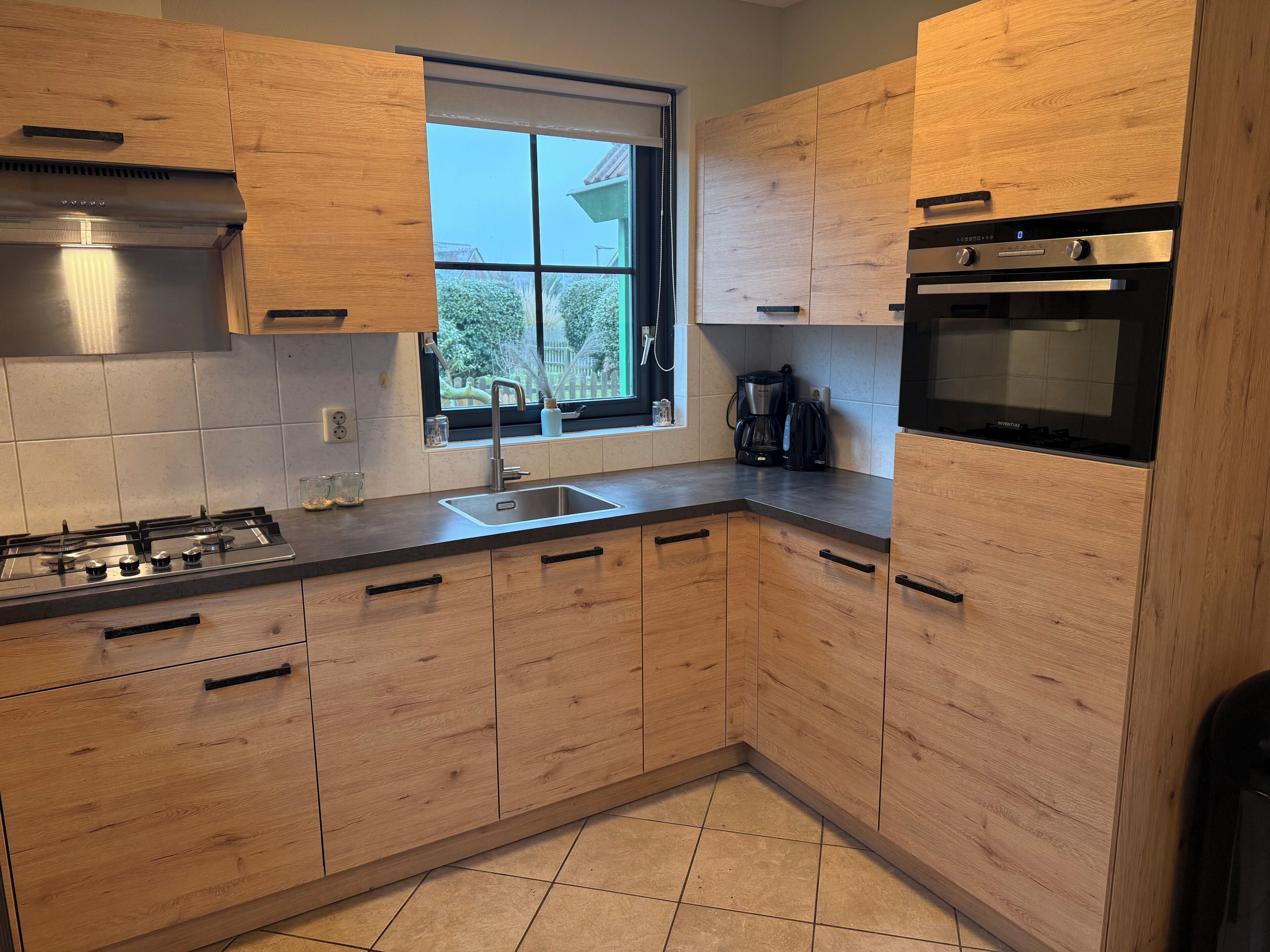 A modern kitchen with wooden cabinets, a gas stove, a sink, and a window with a view of greenery.