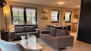 A modern living room with a sofa, armchair, and coffee table, a dining area with chairs, and a kitchen with cabinets and a stove. - 3 bedroom accommodation in Julianadorp aan Zee (Julianadorp aan Zee)