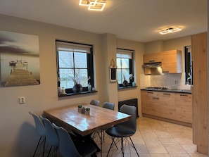 A modern kitchen with wooden cabinets, a dining table with chairs, and a window with a view of a dock. - 3 bedroom accommodation in Julianadorp aan Zee (Julianadorp aan Zee)