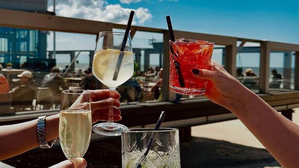 A group of people toasting with drinks at a beachside bar with a flag in the background. - 3 bedroom accommodation in Julianadorp aan Zee (Julianadorp aan Zee)
