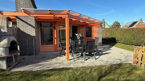 Ein modernes Haus mit Terrasse, einem Steinofen und einer überdachten Außenlounge.