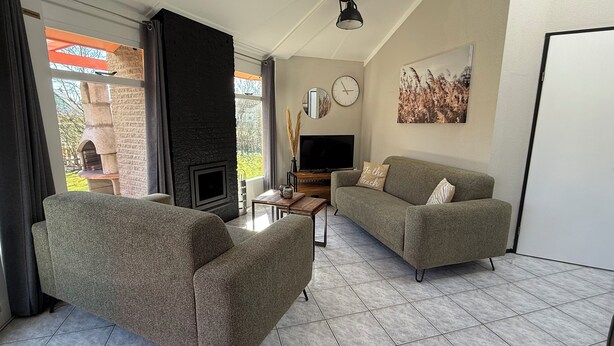 Ein Wohnzimmer mit Kamin, einer Couch, einem Fernseher und Blick ins Freie.