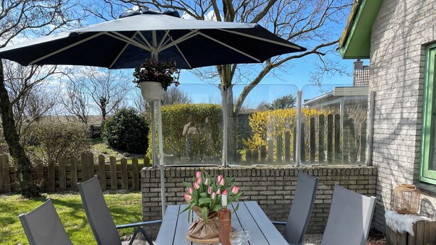 A patio with a table and chairs, a hanging flower pot, and a view of a cemetery. - 2 bedroom accommodation in Julianadorp aan Zee (Julianadorp aan Zee)