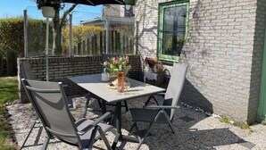 An outdoor patio with a table, chairs, and a hanging flower pot. - 2 bedroom accommodation in Julianadorp aan Zee (Julianadorp aan Zee)