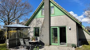 A house with a brick exterior, green trim, and a patio with outdoor furniture. - 2 bedroom accommodation in Julianadorp aan Zee (Julianadorp aan Zee)