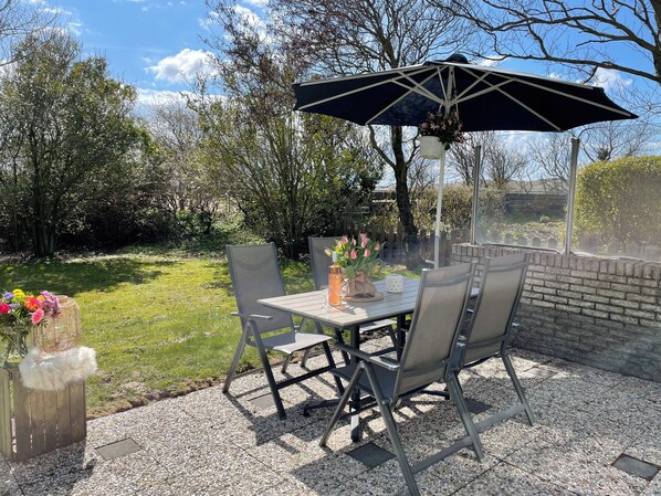 Un patio al aire libre con una mesa, sillas y una sombrilla colgante.
