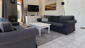 Una sala de estar moderna con un sofá gris, una mesa de centro blanca y un sofá gris. Un televisor de pantalla plana está montado en la pared, y hay un cuadro sobre el sofá.