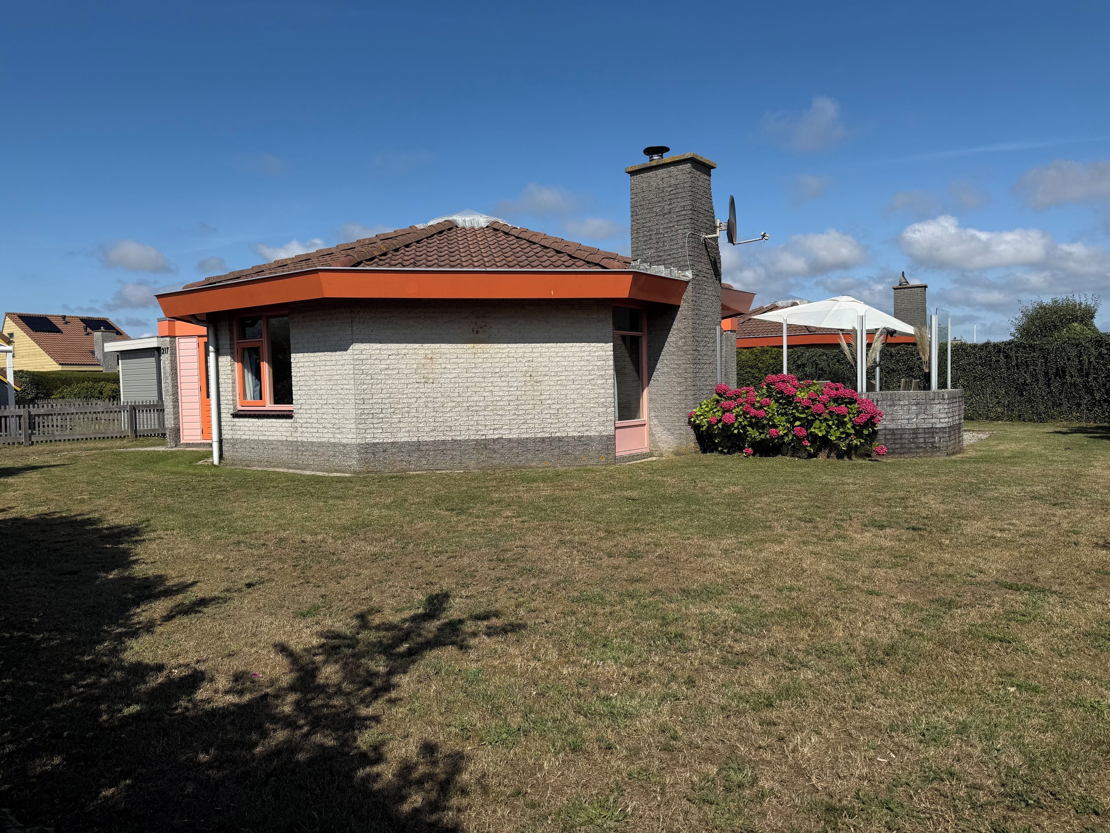 Una casa con facciata in mattoni, un camino e un piccolo giardino con fiori rosa.