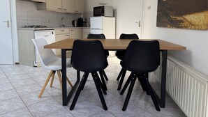 Una cocina moderna con comedor. Incluye una mesa de madera, sillas negras, una silla blanca, un microondas, un refrigerador y un reloj en la pared.