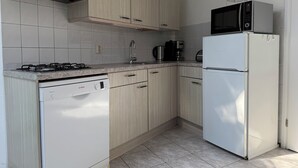 Una cocina moderna con armarios de madera clara, un lavavajillas Bosch, un refrigerador blanco, un microondas y una estufa a gas.