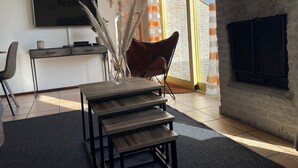 A modern living room with a TV, a wooden coffee table, a red chair, and a large window with curtains. - 3 bedroom accommodation in Julianadorp aan Zee (Julianadorp aan Zee)