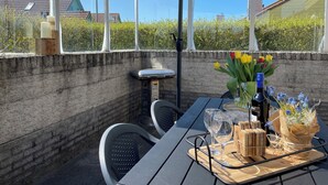 An outdoor dining area with a table, chairs, an umbrella, and a view of a brick wall and greenery. - 3 bedroom accommodation in Julianadorp aan Zee (Julianadorp aan Zee)